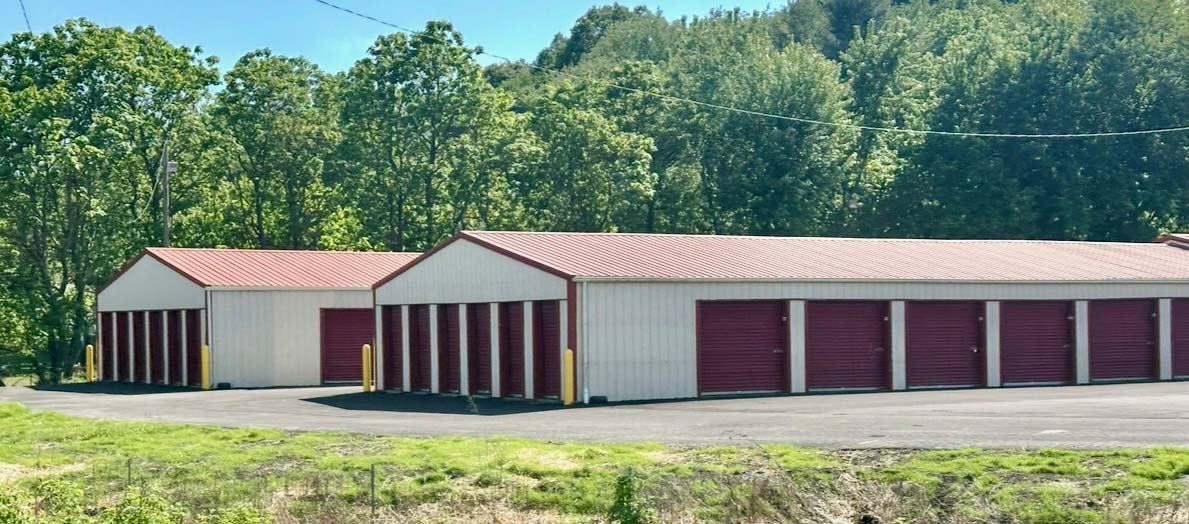 Holliday's Mini Storage facility in Lancaster, Ohio, set against the wooded Fairfield County hillside, with multiple storage buildings visible.