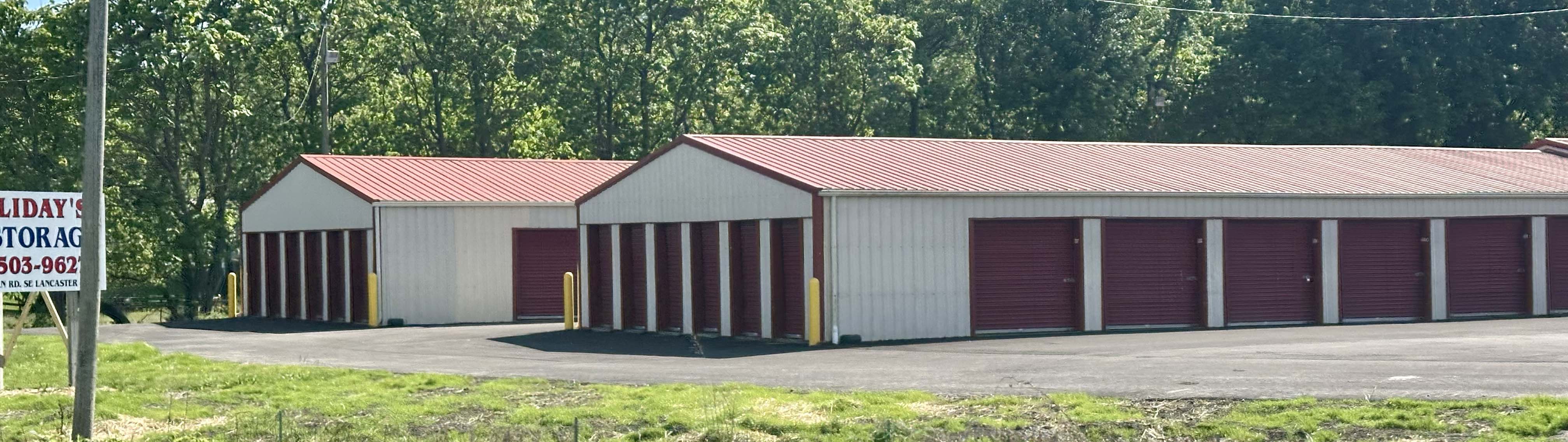Multiple Holliday's Mini Storage buildings from across Old Logan Road with roadside sign in the foreground.